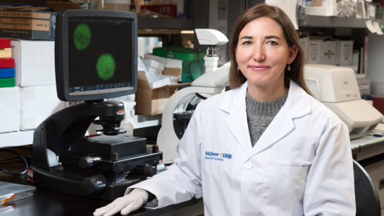 Dr. Crisina Nostro sitting in a lab in front of a microscope