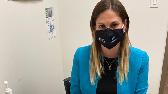 Dr. Mia Bondi, a primary care nurse practitioner in the community and researcher at UHN’s Toronto Centre for Liver Disease sitting at a table with a mask on.