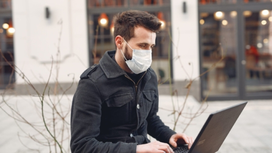 Man with a mask sitting outdoors on his laptop