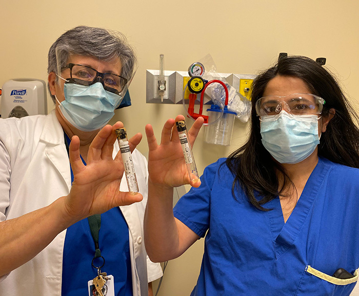 Stella Kozuszko and Yas Moayedi holding vials with PPE on.