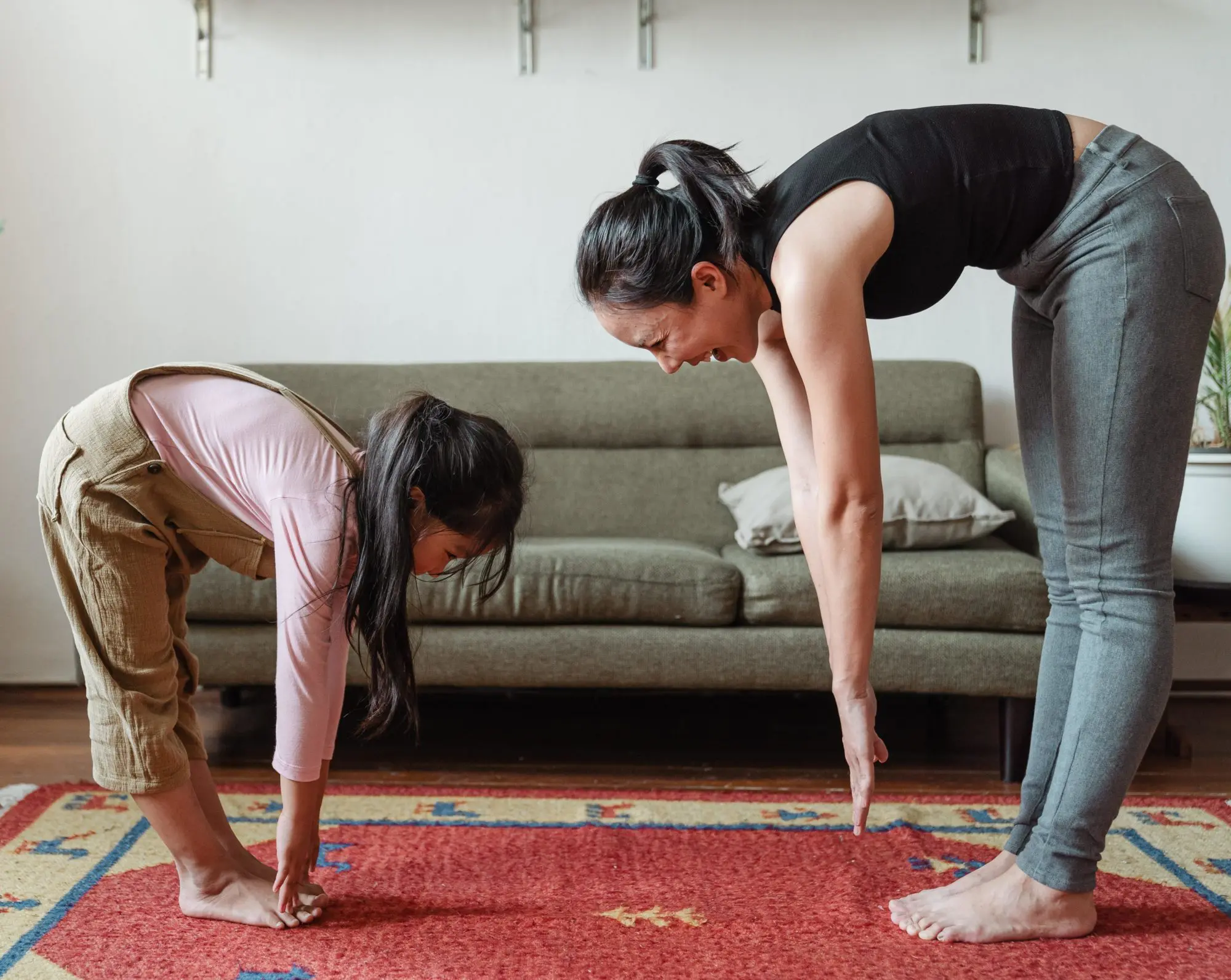 Landscape photo of a mother and daughter stretching (trying to touch their toes) together in the living room.