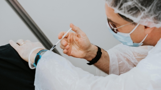 Photo of a doctor wearing PPE and administering a vaccine.