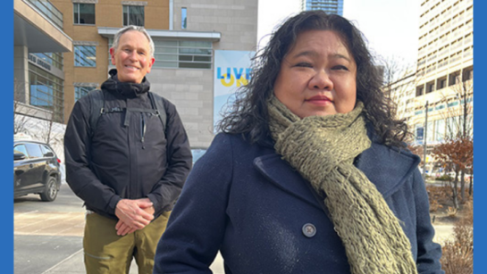 UHN Patient Partners Jack Ireland and Lilac Chow pose outside UHN in their winter jackets and scarves on a cloudy day