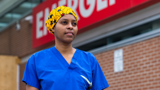 Patrice Wedderburn shown outside the Toronto Western Hospital Emergency Department sign on a cloudy day while wearing blue scrubs and a yellow head cap.