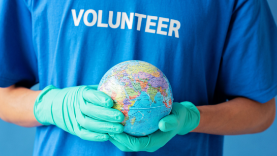 A volunteer wearing a blue shirt that says volunteer and holding a globe in their hands while wearing teal rubber gloves