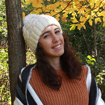Camila Lima smiles outside in the fall with a scarf and winter hat.