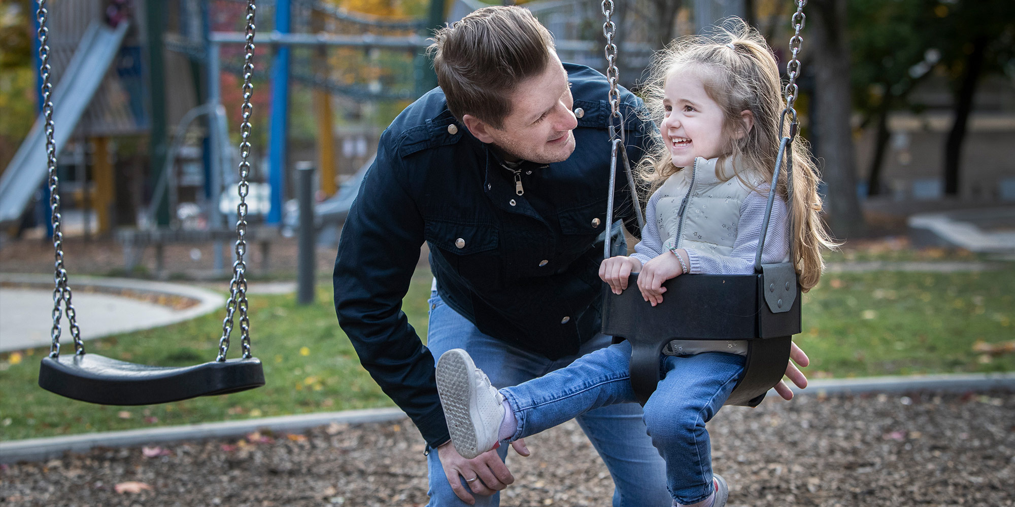 Photo: a father pushes his young daughter in a swing at the park.