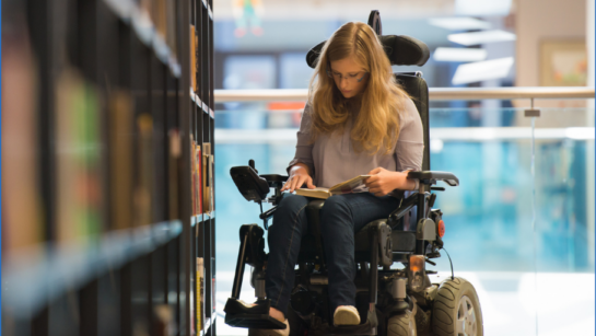 A young woman browses books at a library in a wheelchair