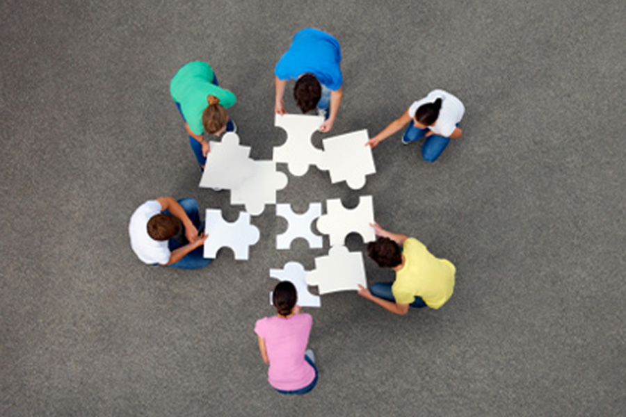 Students try to piece together a giant jigsaw puzzle on a carpet.