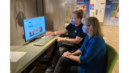 Two individuals sit at a computer and browse online resources at UHN