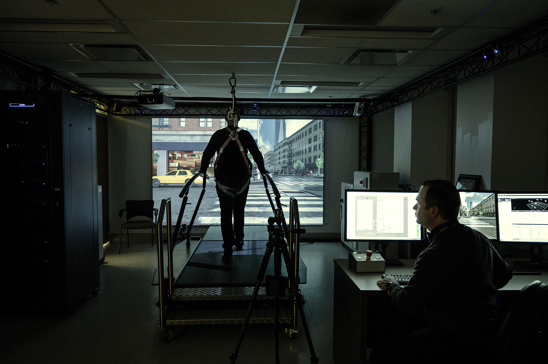 Kinesiologist monitoring a patient strapped in a safety harness inside the Gait Lab experiencing the immersive rehabilitation research space.