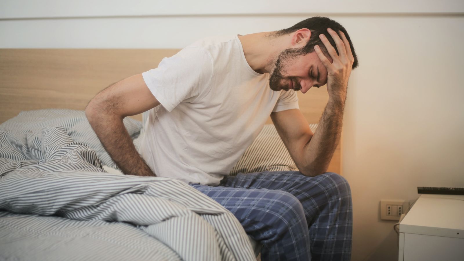 A person grabbing their head while getting up from bed