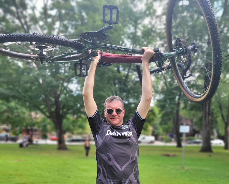 John Richmond holding his bike over his head at a park.