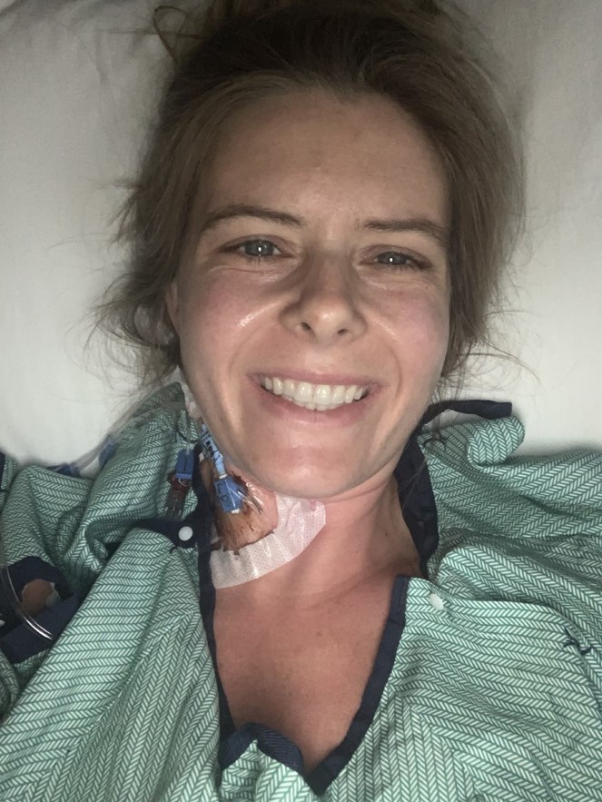 Meredith Burns taking a selfie while in a hospital gown smiling.