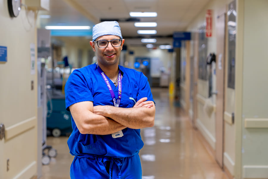 Dr. Amin Madani, in surgical scrubs while smiling in a hallway at UHN.