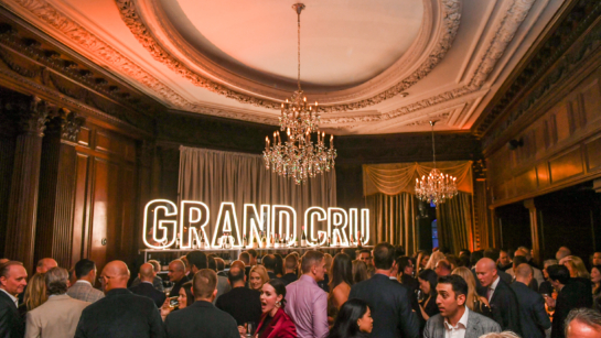 Guests mingling in a ball room in front of a large light up GRAND CRU sign