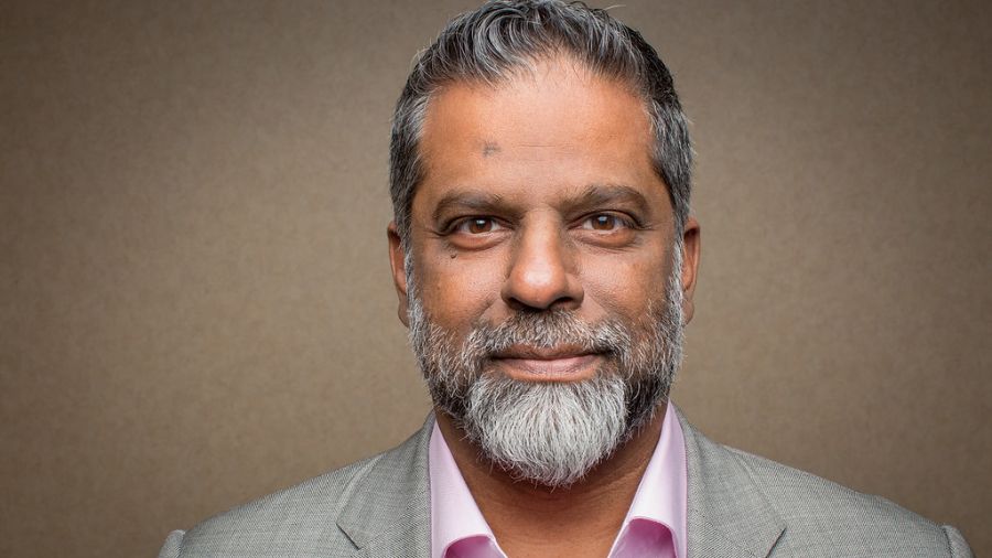 Raja Rampersaud wearing a suit and smiling for the camera in a close up photo.