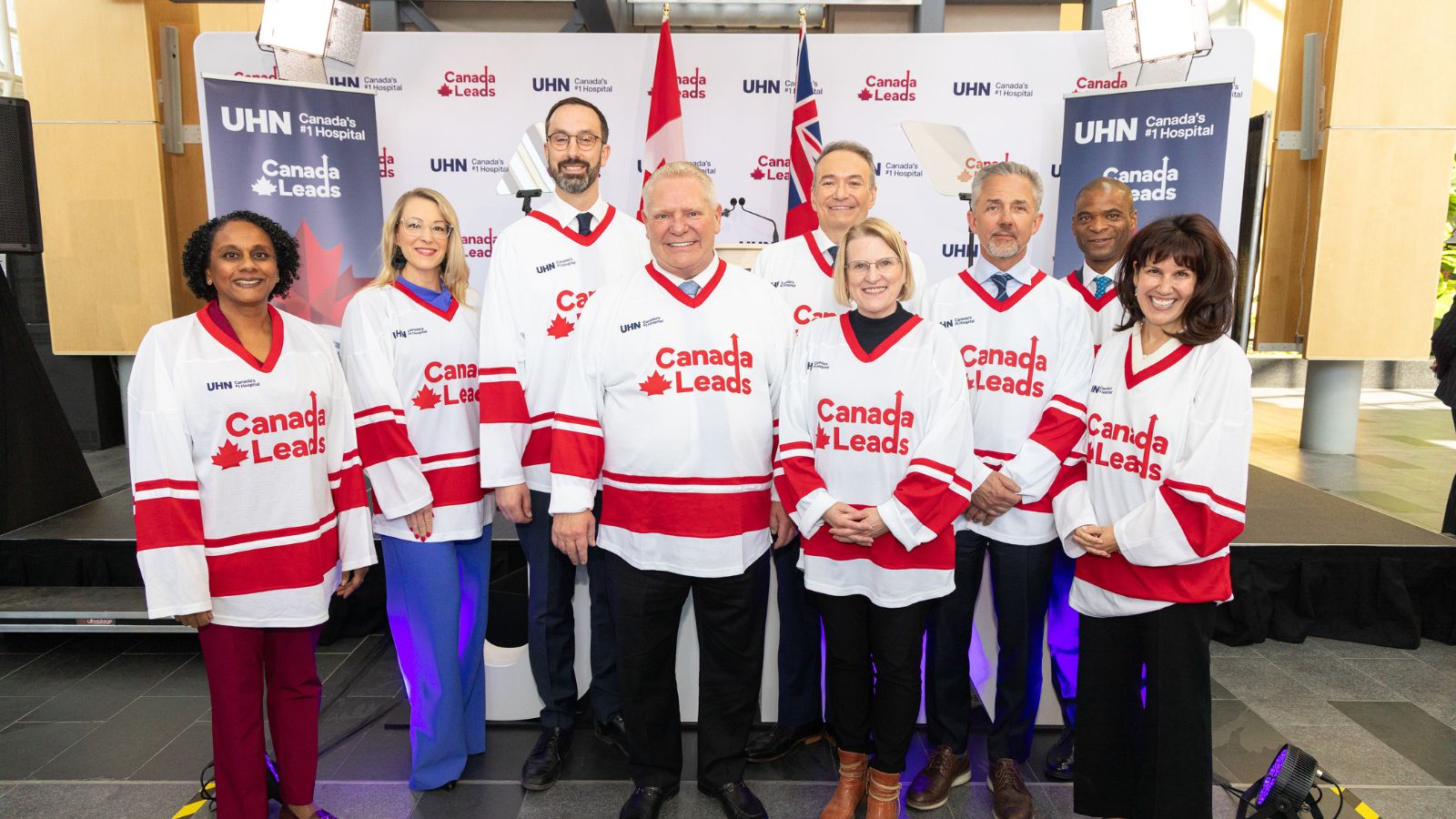 Speakers at the launch of the Canada Leads 100 Challenge at UHN’s Toronto General Hospital in a group photo on stage.