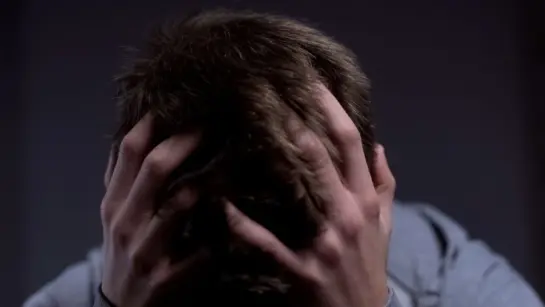 A person grabs their head with a dark background.