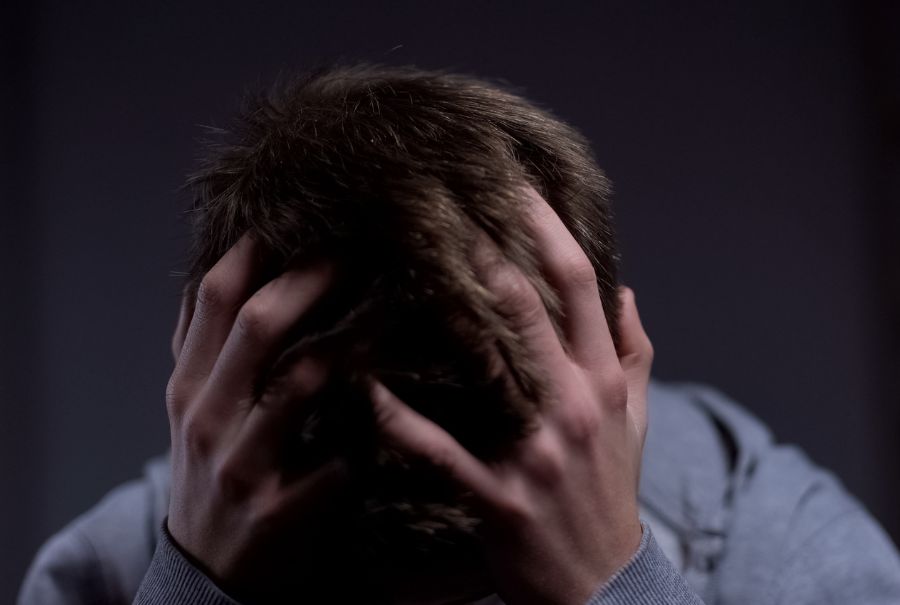 A person grabs their head in pain with a dark background.
