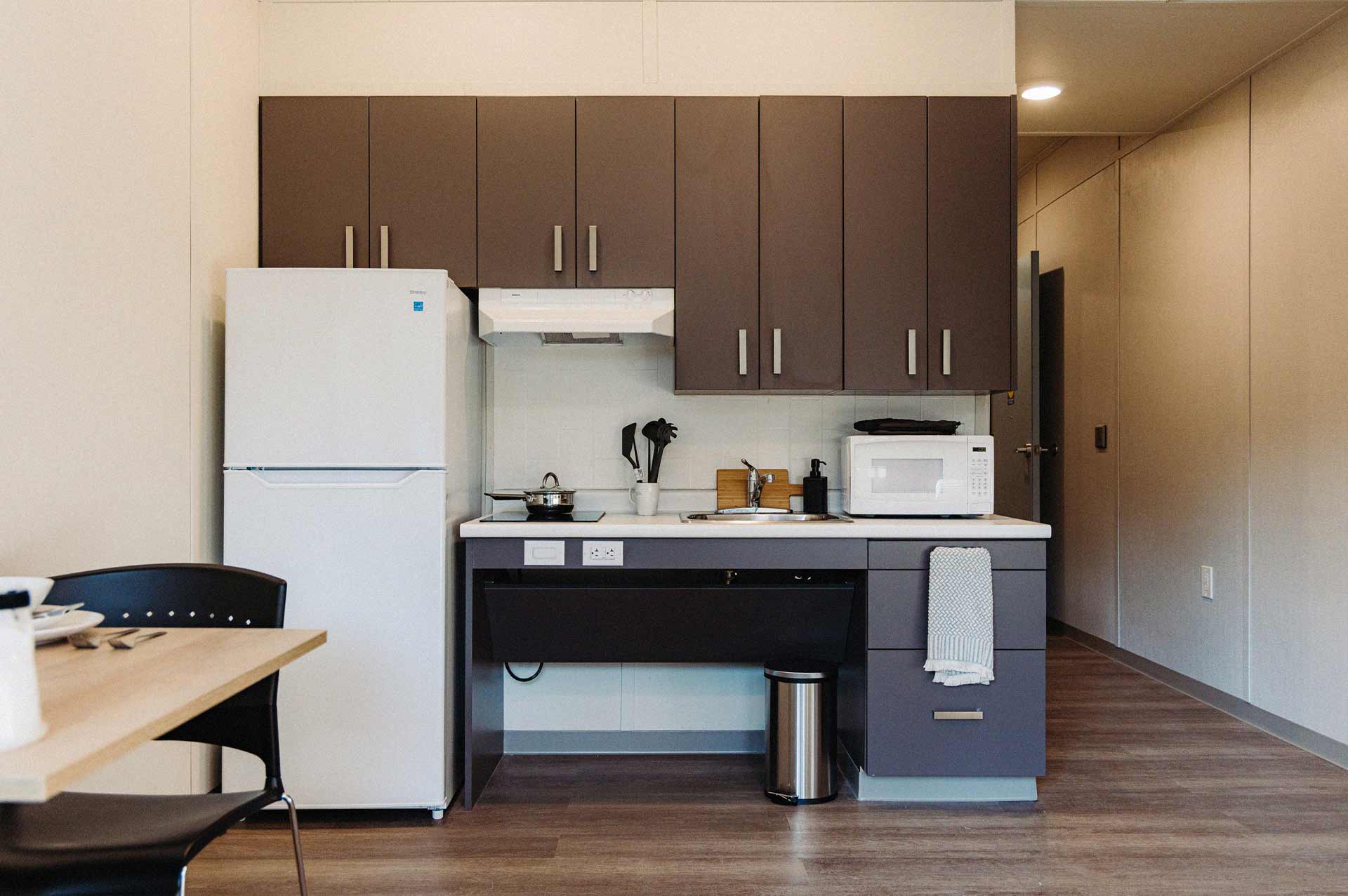 A kitchenette in Dunn house, showcasing a fridge, counter with microwave and table, and chairs.