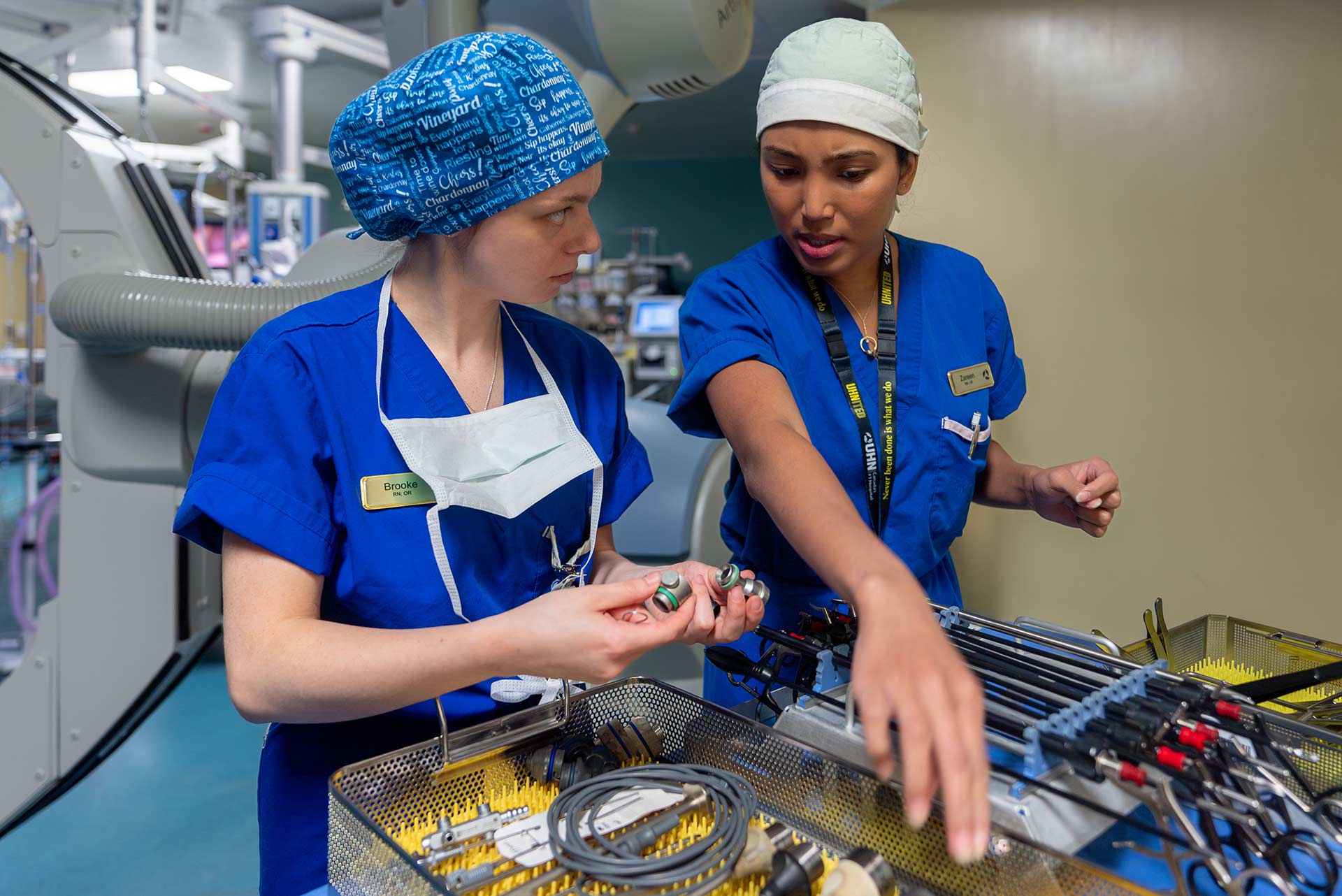 Two nurses in an operating room, standing over surgical tools.