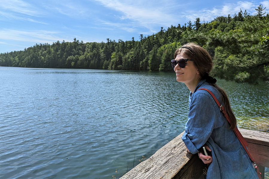 ​Stephanie MacAlpine leaning against a railing while overlooking a lake with trees lining the coast. (Photo courtesy of Stephanie MacAlpine)