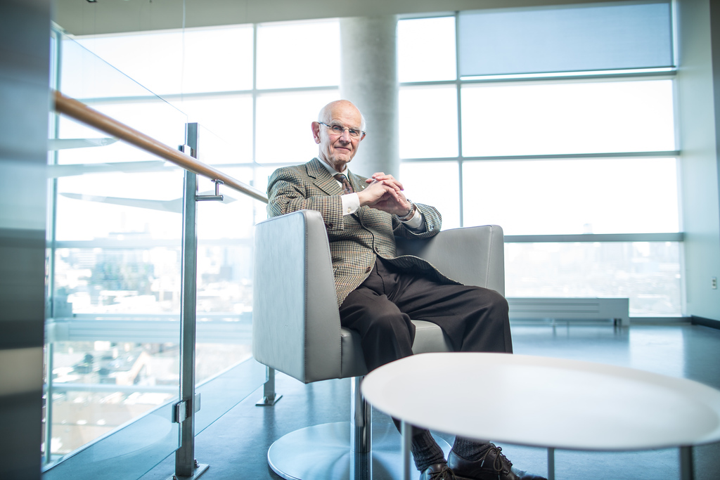 Dr. Charles Tator in a bright room sitting with his fingers crossed.