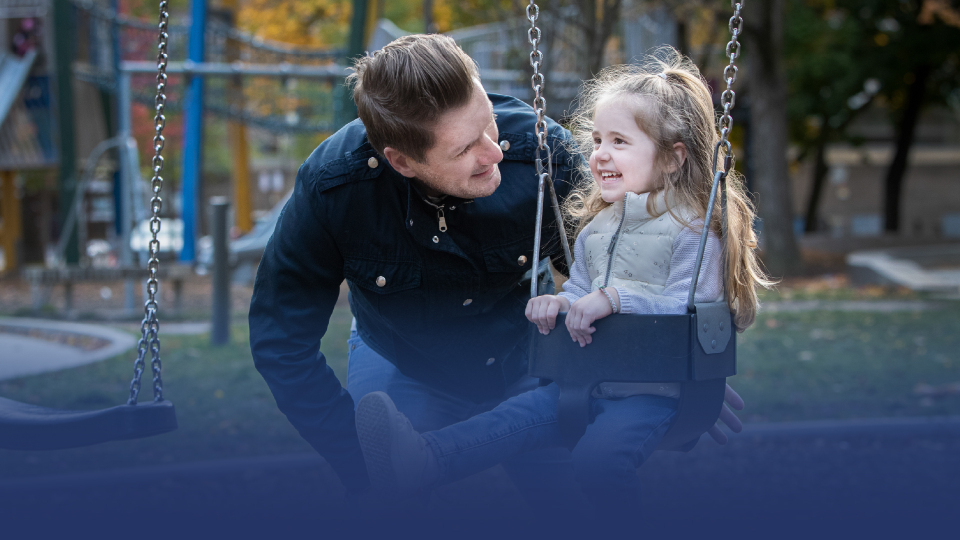 A father and daughter having fun on a swingset.
