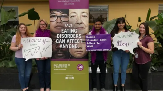 NEDIC staff standing next to a poster and holding signs about eating disorders.