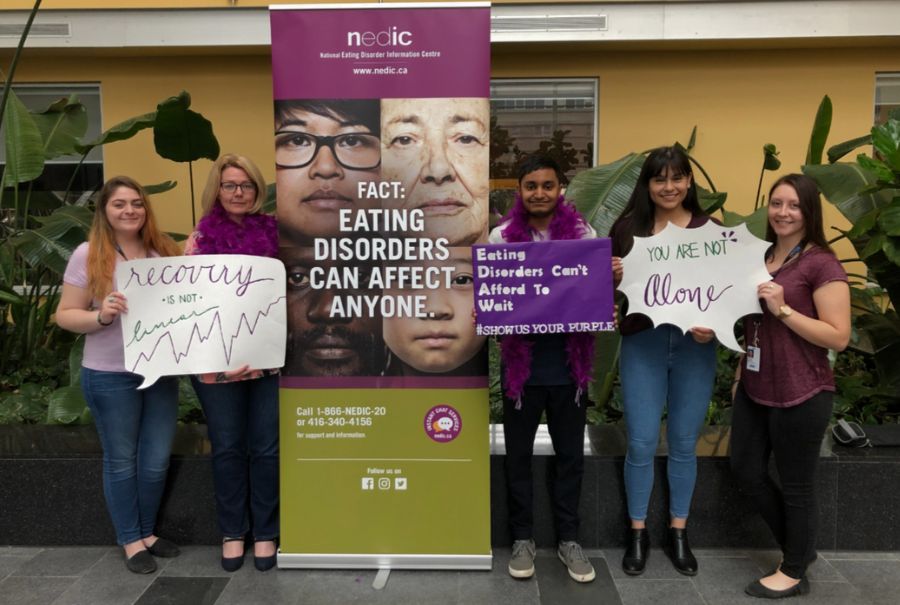 NEDIC staff standing next to a poster and holding signs about eating disorders.