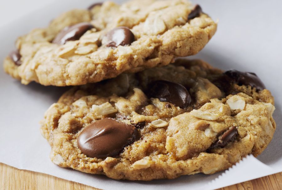 Oatmeal chocolate chip cookies on a table with some chocolate chips next to them. 
