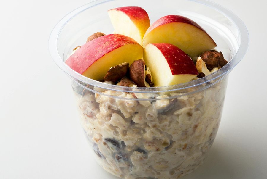 Overnight oats in a plastic cup with apples and walnuts on top.