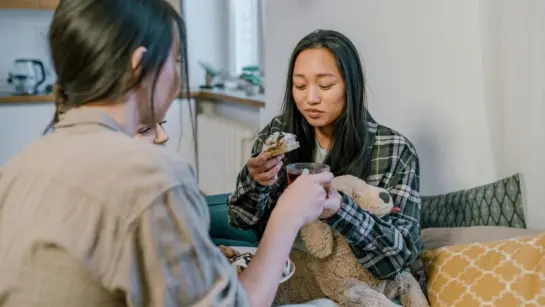 Two people on a couch enjoying snacks and talking.