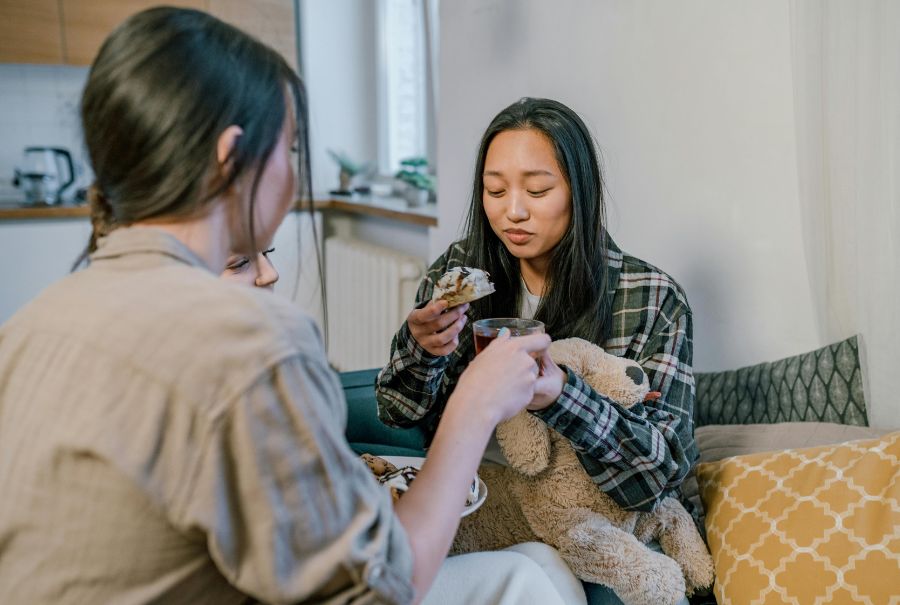 Two people on a couch enjoying snacks and talking.