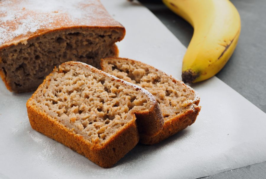 Banana bread on a white cutting board with a banana next to it. 