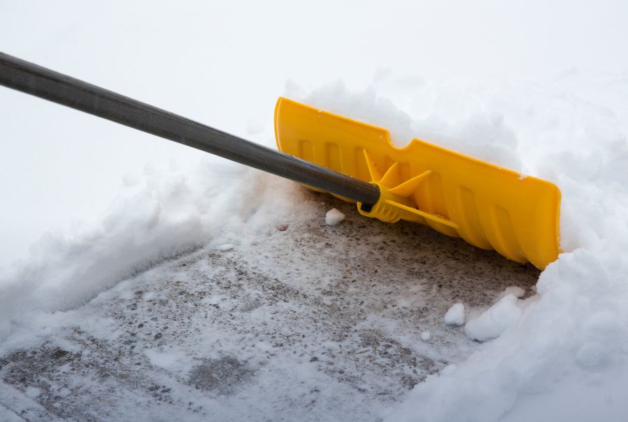 A yellow shovel pushing snow and clearing a path. 