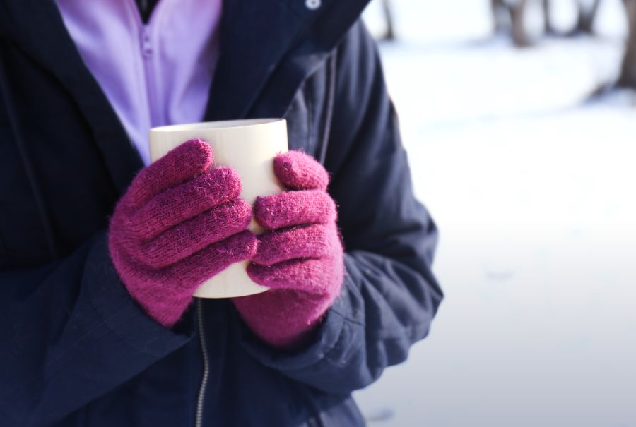 A person outdoors in the snow holding a hot beverage with gloves on.