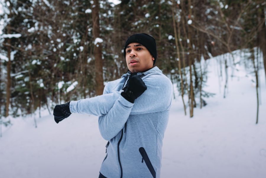 A person stretching their arms outdoors. There are trees in the background.