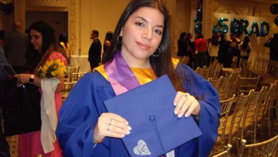 Maria at her graduation in her gown and holding a graduation hat.