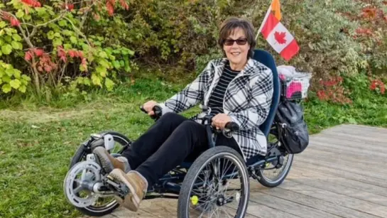 Lisa Carnevale on a specialized bike in front of bushes and with a Canadian flag.