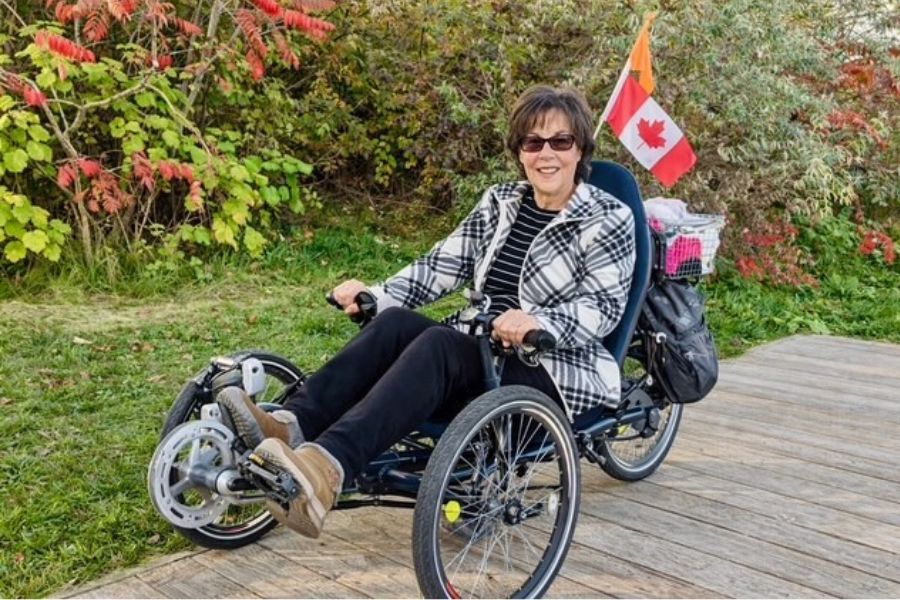 Lisa Carnevale on a specialized bike in front of bushes and with a Canadian flag.