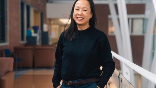 Esther Bui at Toronto Western Hospital with her hands in her pockets and smiling next to a railing.