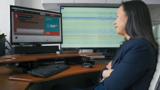 Dr. Esther Bui sitting at a desk listening to a lullaby and looking at brain waves on a separate monitor.