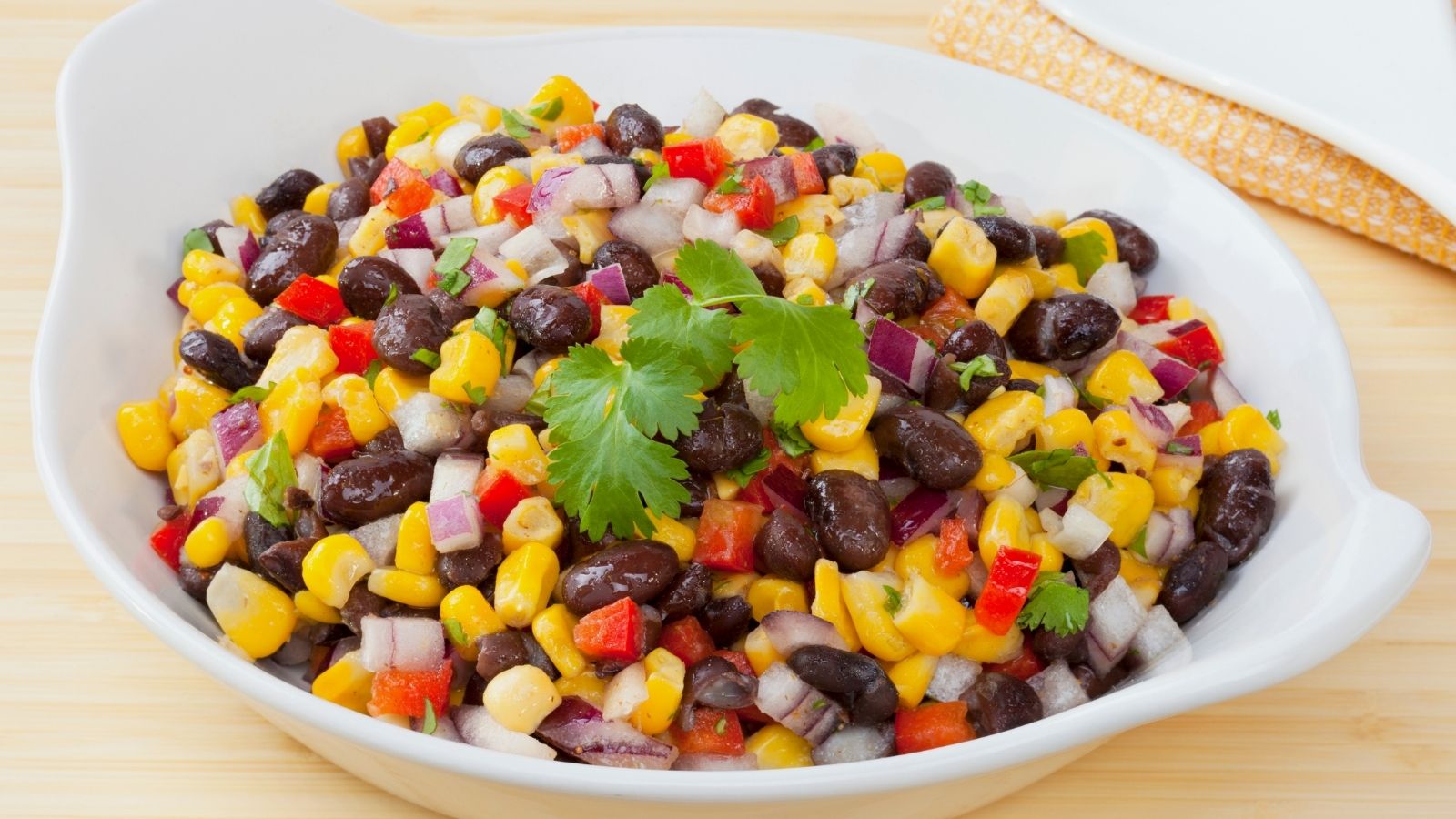 Black bean and corn salad in a white dish and light wood table.
