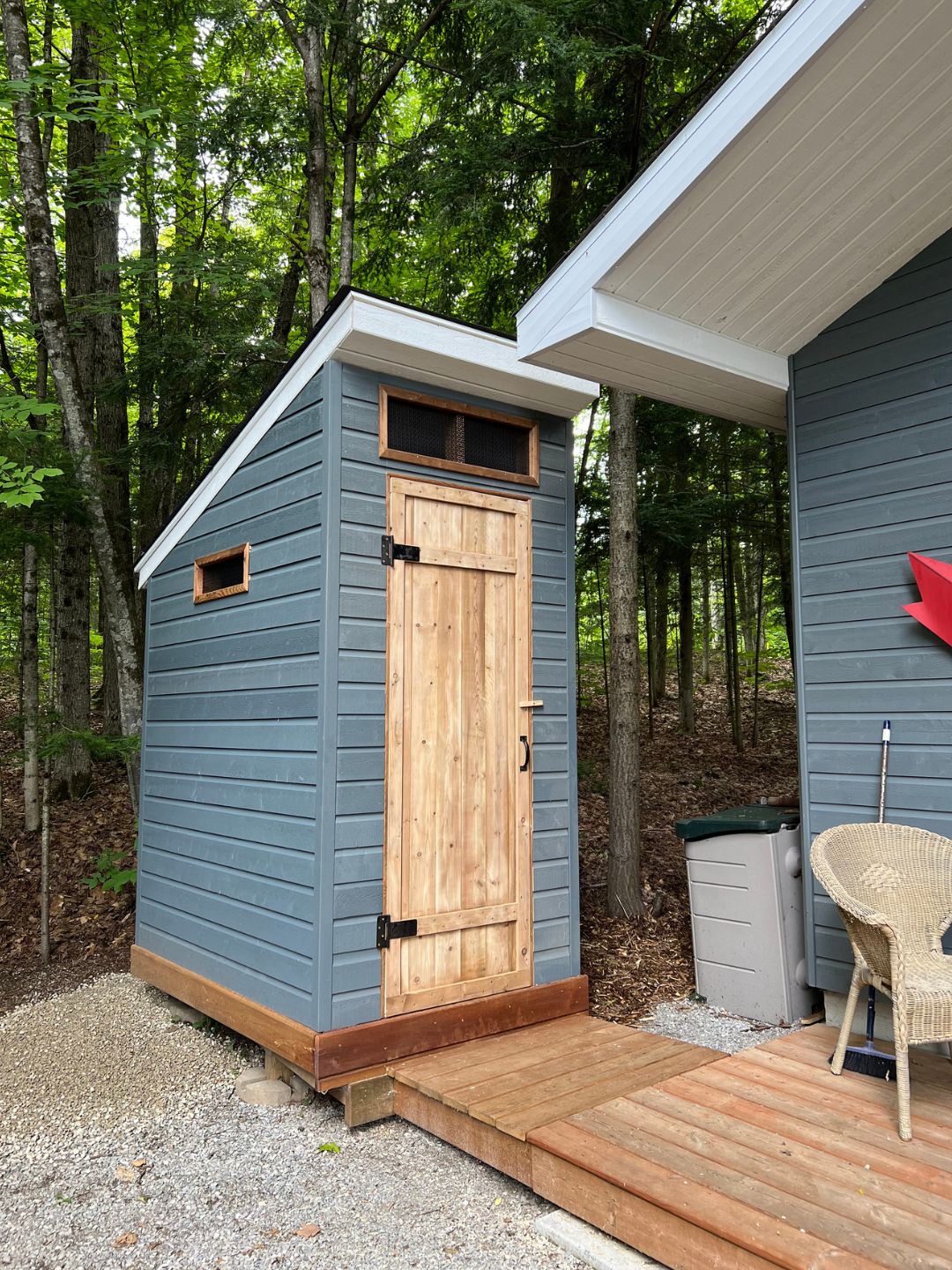 An bran new outhouse with windows and a wood door, painted with a blue/grey colour. 