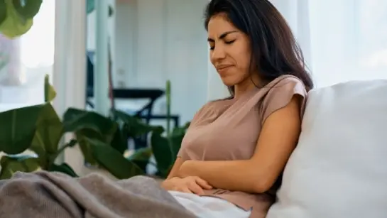 A lady holding her stomach while sitting on the couch.