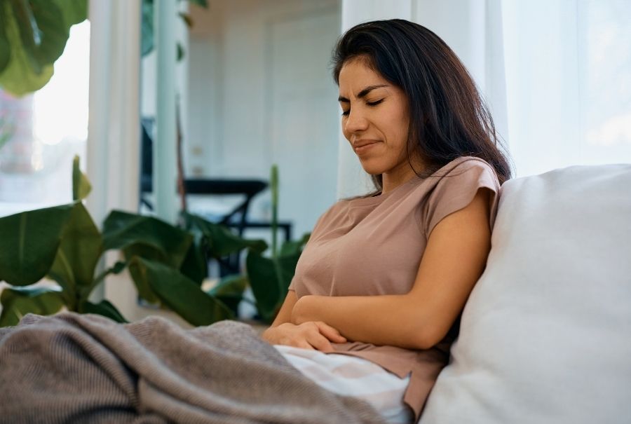 A lady holding her stomach while sitting on the couch.