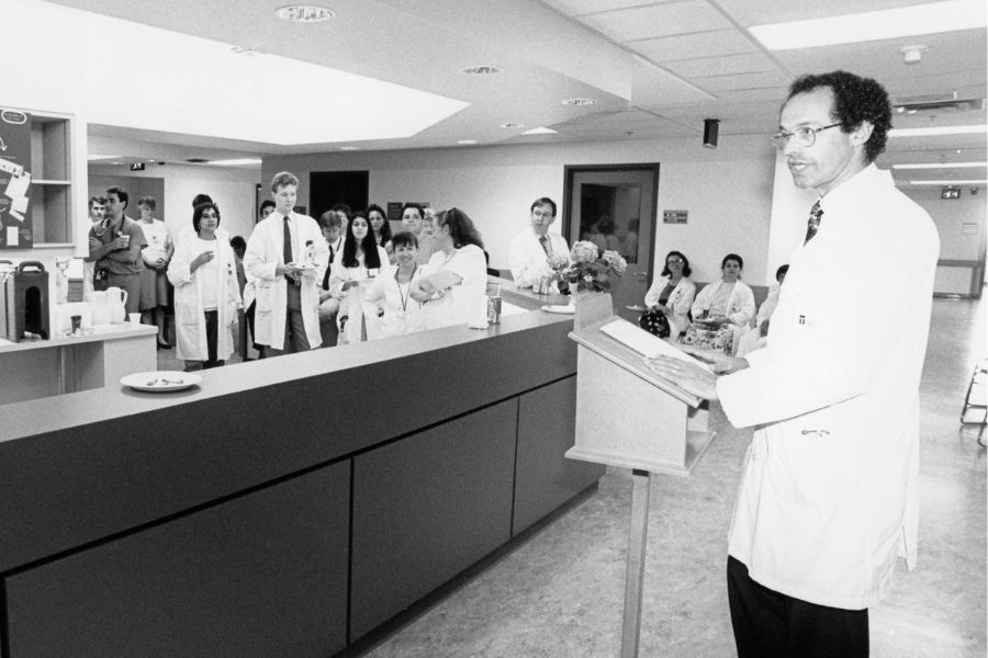 A black and white photo pictured in 1992 of Dr. Michael Baker at a lectern in front of hospital staff.