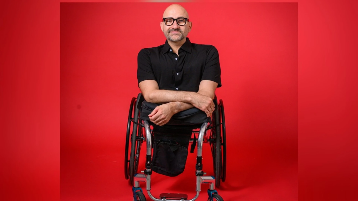 Professional headshot of Spencer West smiling in a black button down against a red backdrop